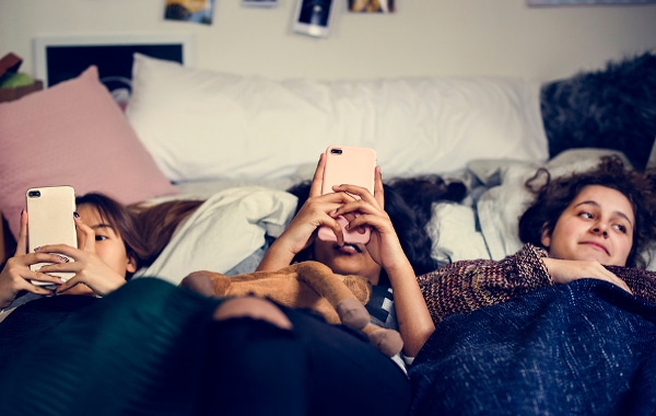 Three teen girls lying down using their phones.