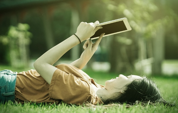 Teenager lying down in the grass using a tablet.