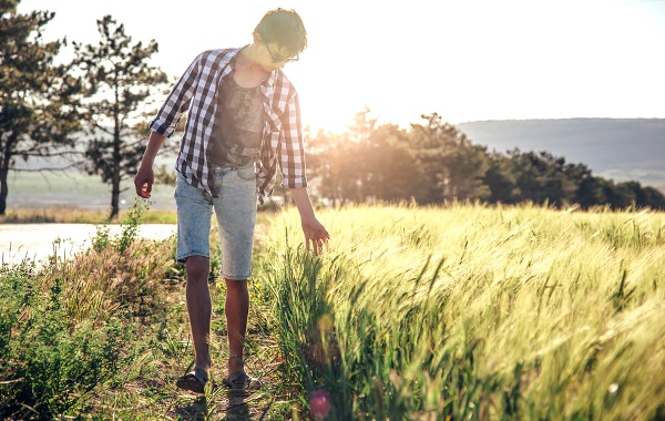 Teenage boy walking on a pathway with tall grass to the side.