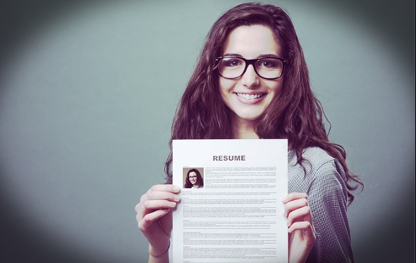 Young woman holding up a resume smiling.