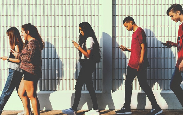 Group of teenagers walking and using their smartphones.