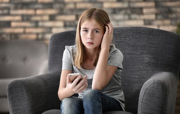 Young teenage girl sitting in a grey chair with a mobile phone.