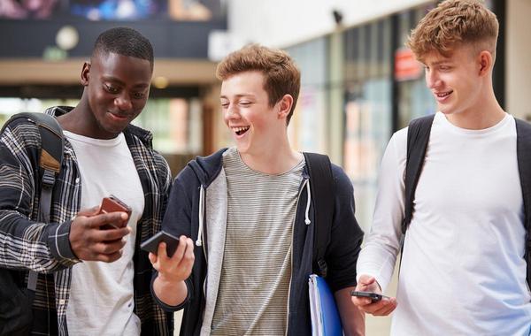 Group of three teen boys looking at and using their phones.