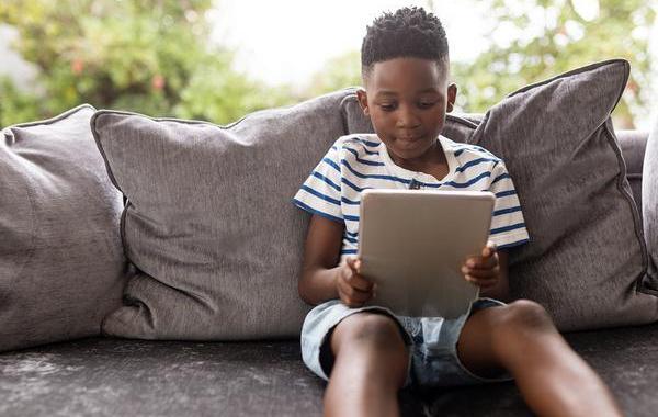 Young teen boy sitting on a couch looking at a tablet.