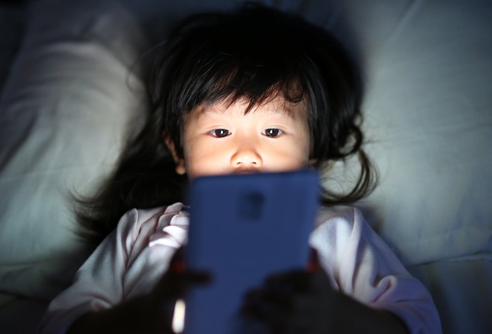 A young girl plays on a smartphone at bed during the night