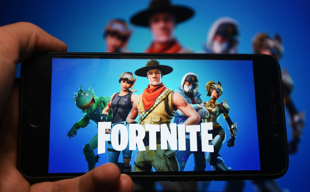 The game Fortnite appears on a smartphone with the Fortnite graphics in the background