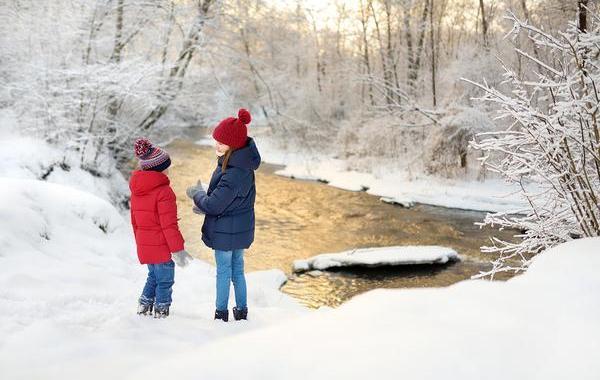 Two young teens outside near a brook in the winter with snow.