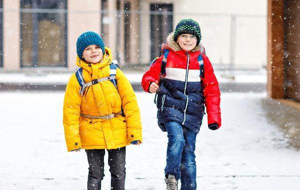 Two young teens walking down the sidewalk wearing winter clothes.