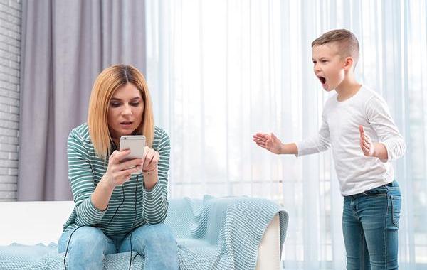 Child yelling at mom while she is looking at her parental control app on her phone.