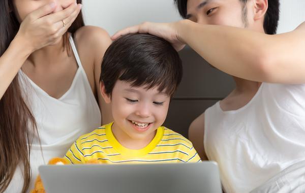 Parents sitting behind their child while he is looking at his laptop computer.
