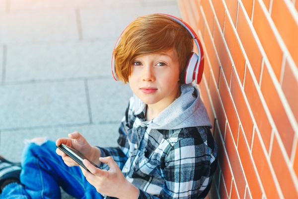 Young teen wearing headphones while sitting on the ground using a phone.