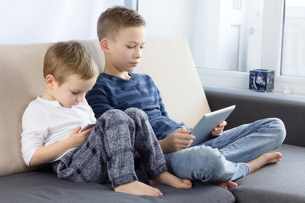 Brothers sitting on a couch each using tablets.