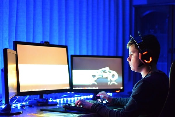 Teen sitting at his desk with three monitors and a headset.
