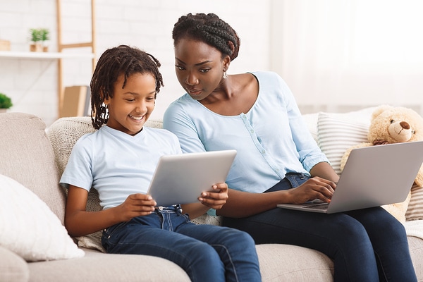 Mother and teen daughter sitting on a couch with laptops.