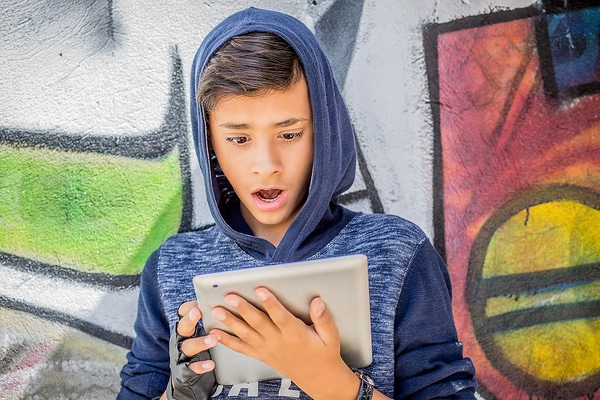 Young teen with a surprised look on his facing while looking at his tablet.
