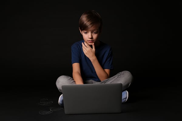 Young teen sitting on the floor looking at a laptop screen.