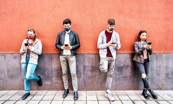 Group of teens leaning against a wall using their phones.