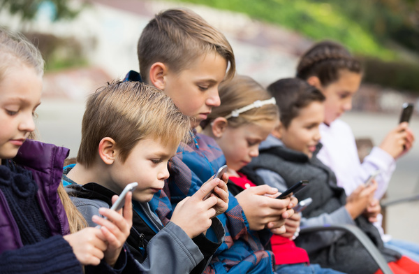 Group of kids sitting outside with phones.